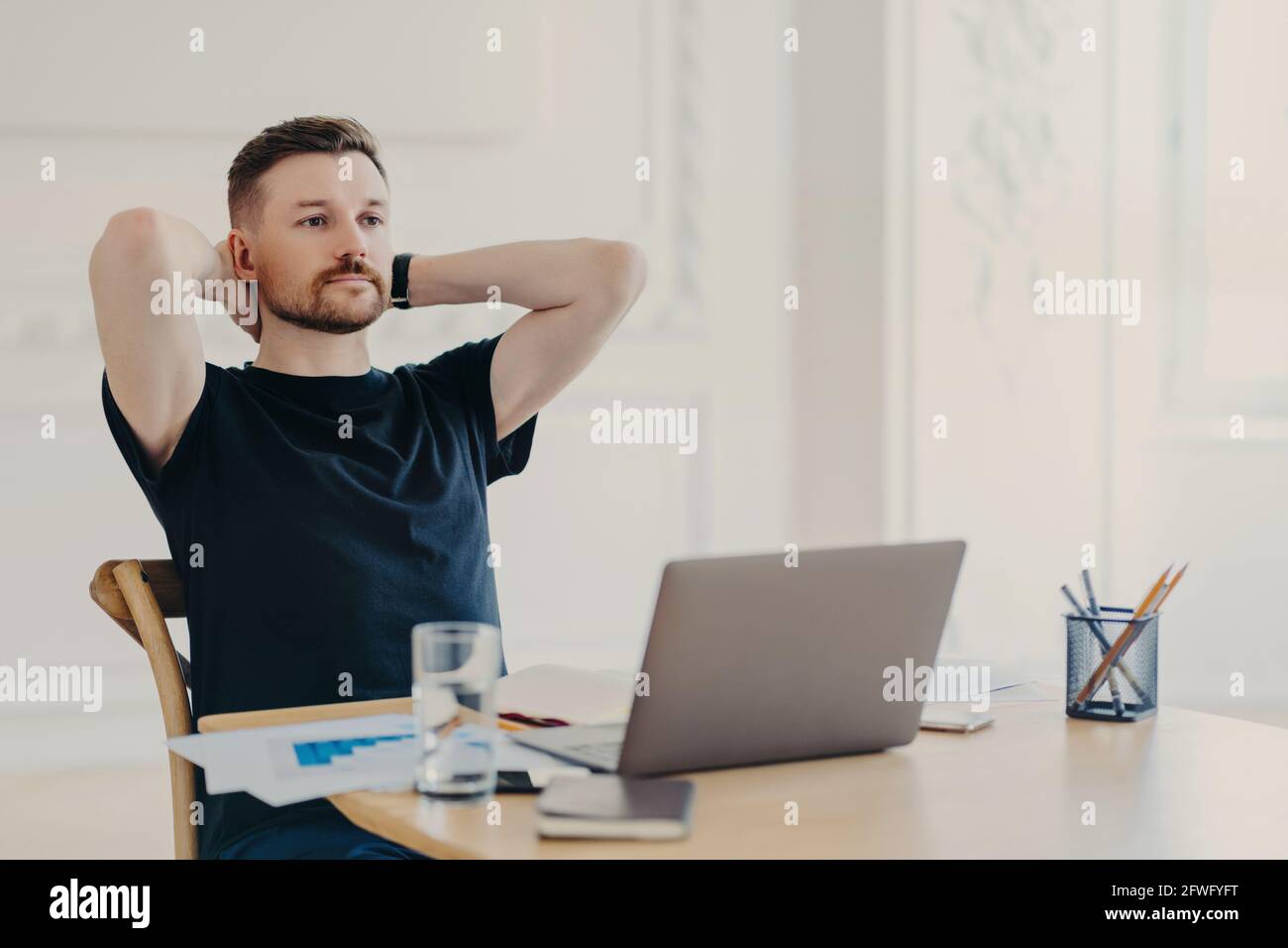 Giovane uomo d'affari che gode di lavoro fatto mentre si siede sul suo posto di lavoro con computer portatile Foto Stock