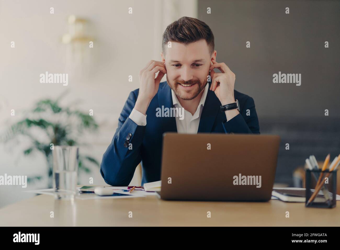 Attraente uomo d'affari che tiene la conferenza di fotoricettore, usando il laptop e gli auricolari Foto Stock