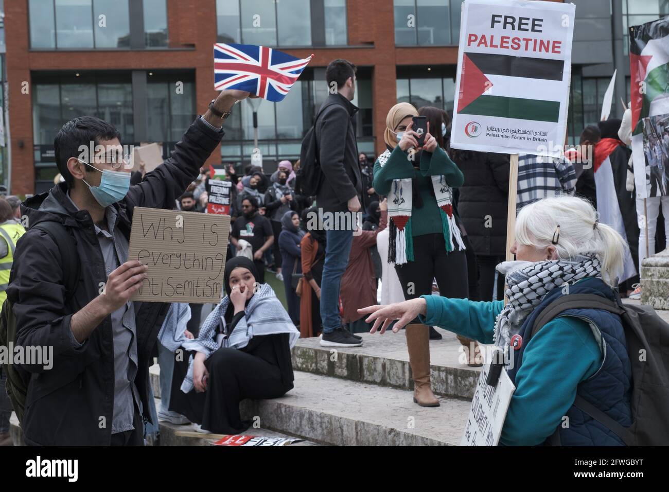 Lady discute con un manifestante che sventolava Union Jack mentre i manifestanti si riunivano ai Piccadilly Gardens, Manchester UK. La dimostrazione è iniziata alle 12 del 22 maggio 2021. La protesta doveva dare sostegno al popolo palestiano e contro la recente escalation del conflitto nella regione. In Palestina il popolo palestinese ha dovuto affrontare un conflitto di sbarramento da Israele a seguito di razzi lanciati da Gaza dal gruppo militante Hamas al potere. Il cessate il fuoco è iniziato all'inizio di venerdì 20 maggio 2021, portando alla fine 11 giorni di combattimenti in cui sono state uccise più di 250 persone, la maggior parte delle quali a Gaza. Foto: ALVAROVELAZQUEZ/ Foto Stock