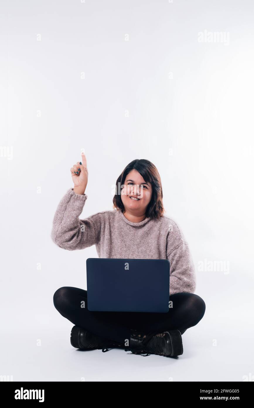 La donna con un computer portatile seduto sul pavimento è rivolta verso l'alto con l'addebito su sfondo bianco. Concetto di shopping. Spazio di copia Foto Stock