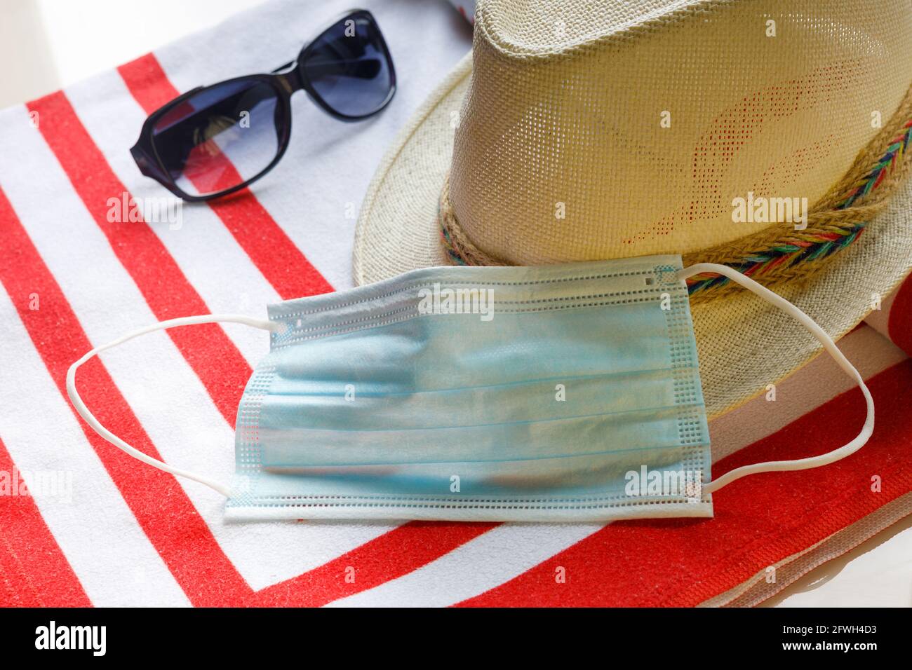 Stagione delle vacanze, pandemia di coronavirus nelle aree ricreative, cappello di paglia, maschera antivirale, occhiali da sole da donna, telo da spiaggia, Concetto di viaggio estivo in sanitar Foto Stock