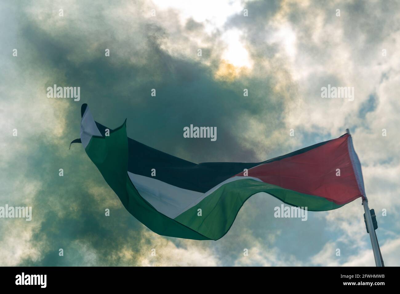 Bandiera dello Stato di Palestina è volata durante una protesta con fumo verde da una luce che blocca la luce solare Foto Stock