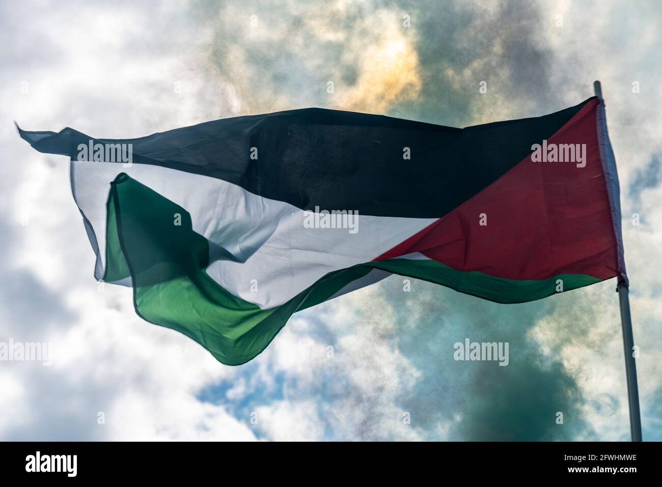Bandiera dello Stato di Palestina è volata durante una protesta con fumo verde da una luce che blocca la luce solare Foto Stock
