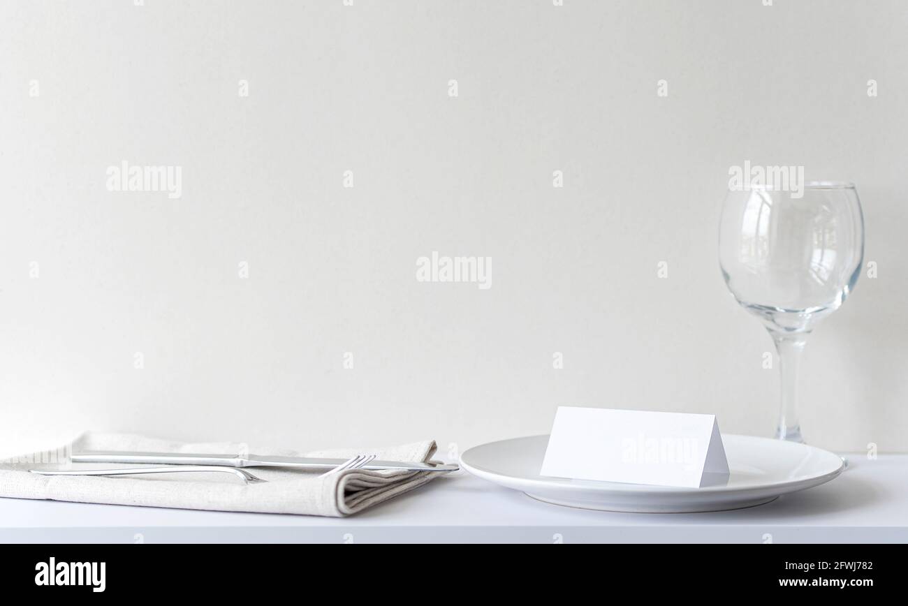 Carta d'invito vuota sul piatto bianco del ristorante. Interno del ristorante con tavolo, posate prima di festeggiare, mockup, spazio per il testo Foto Stock