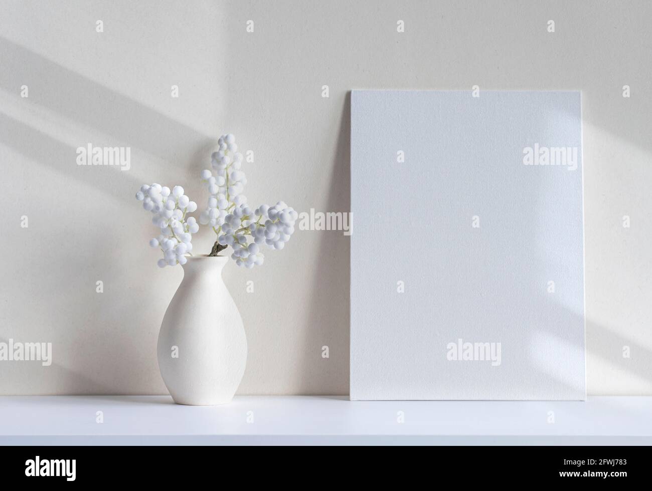 Luce del sole con ombre e linee su tela vuota o foglio, vaso, piante decorative della casa su una scrivania. Interni bianchi, minimal mockup con spazio per Foto Stock