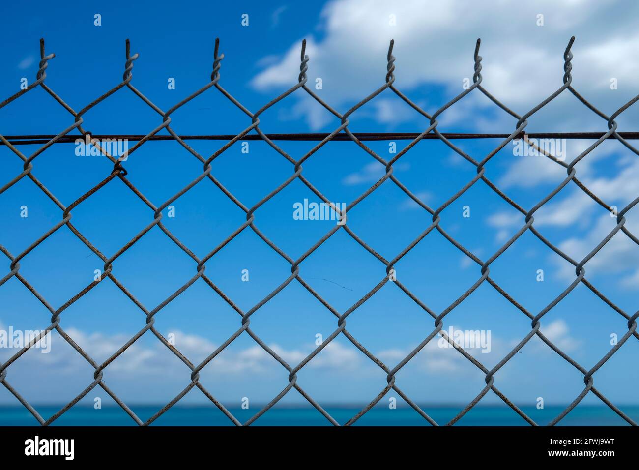 Mare e cielo blu dietro una recinzione a catena Foto Stock