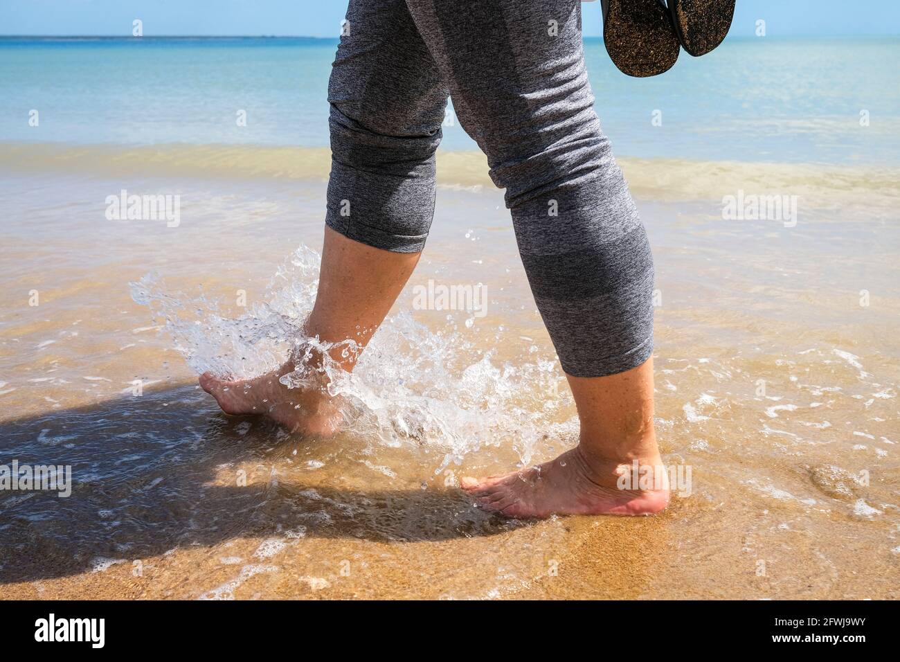 Gambe e piedi di una donna che cammina in acqua in spiaggia Foto Stock Gambe e piedi di una donna che cammina in acqua in spiaggia Foto Stock