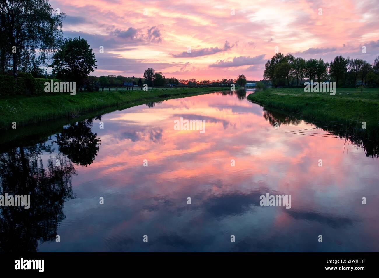 Bella cornice di sole con nuvole colorate e i riflessi nell'acqua del fiume chiamato 'il Dinkel' in viola, magenta, giallo, arancione e blu Foto Stock