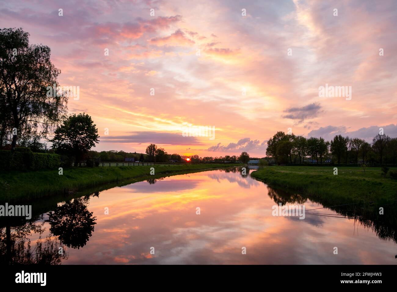 Bella cornice di sole con nuvole colorate e i riflessi nell'acqua del fiume chiamato 'il Dinkel' in viola, magenta, giallo, arancione e blu Foto Stock