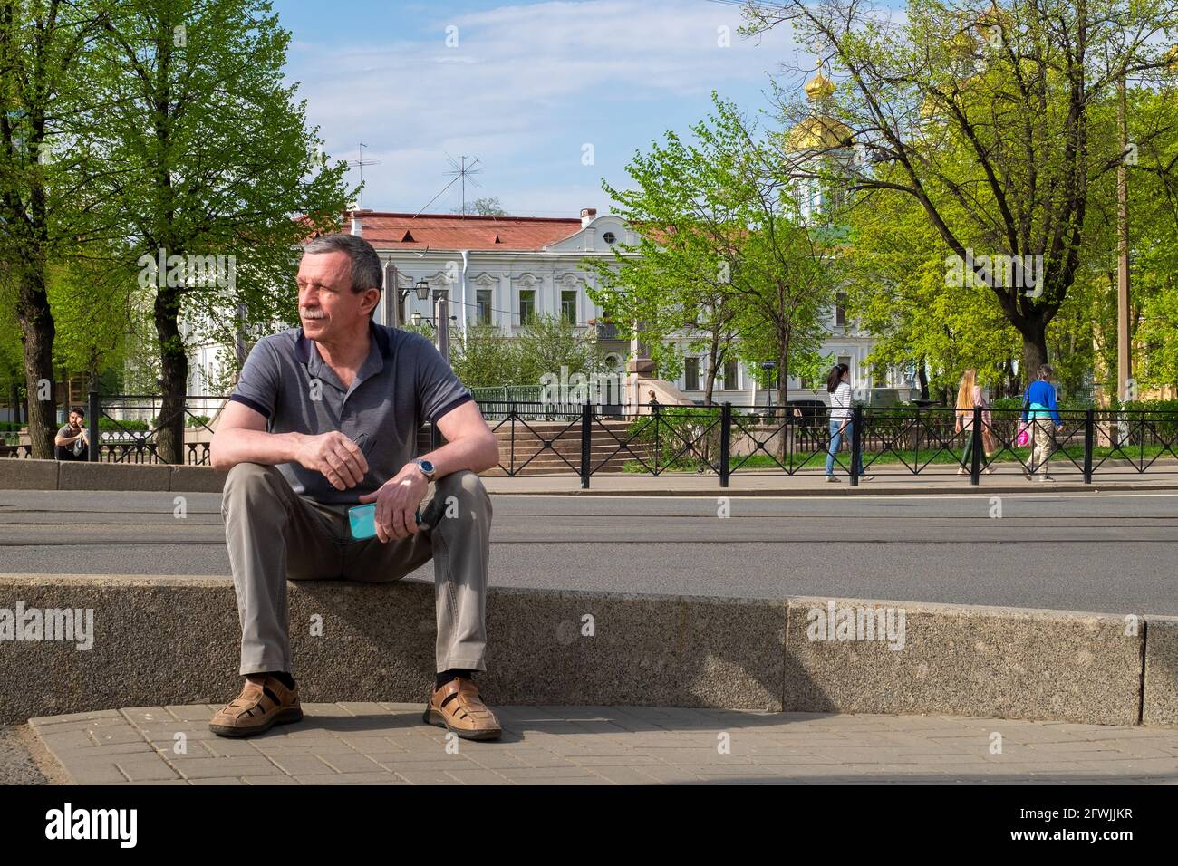 Un uomo caucasico adulto in una T-shirt grigia si siede e. si appoggia sul marciapiede Foto Stock