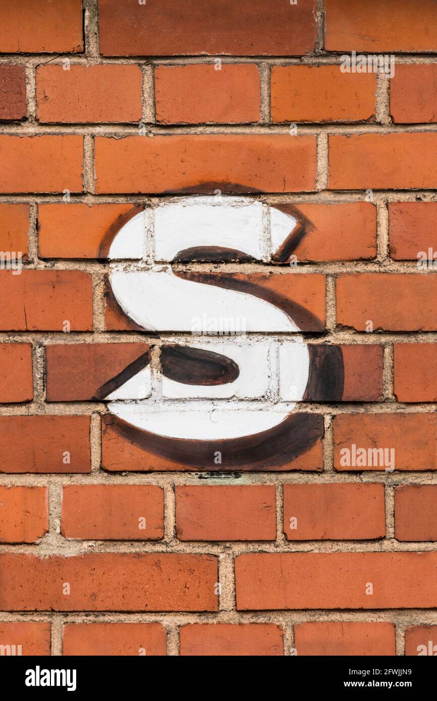 Una lettera bianca s dipinta su un muro di mattoni rossi Foto Stock