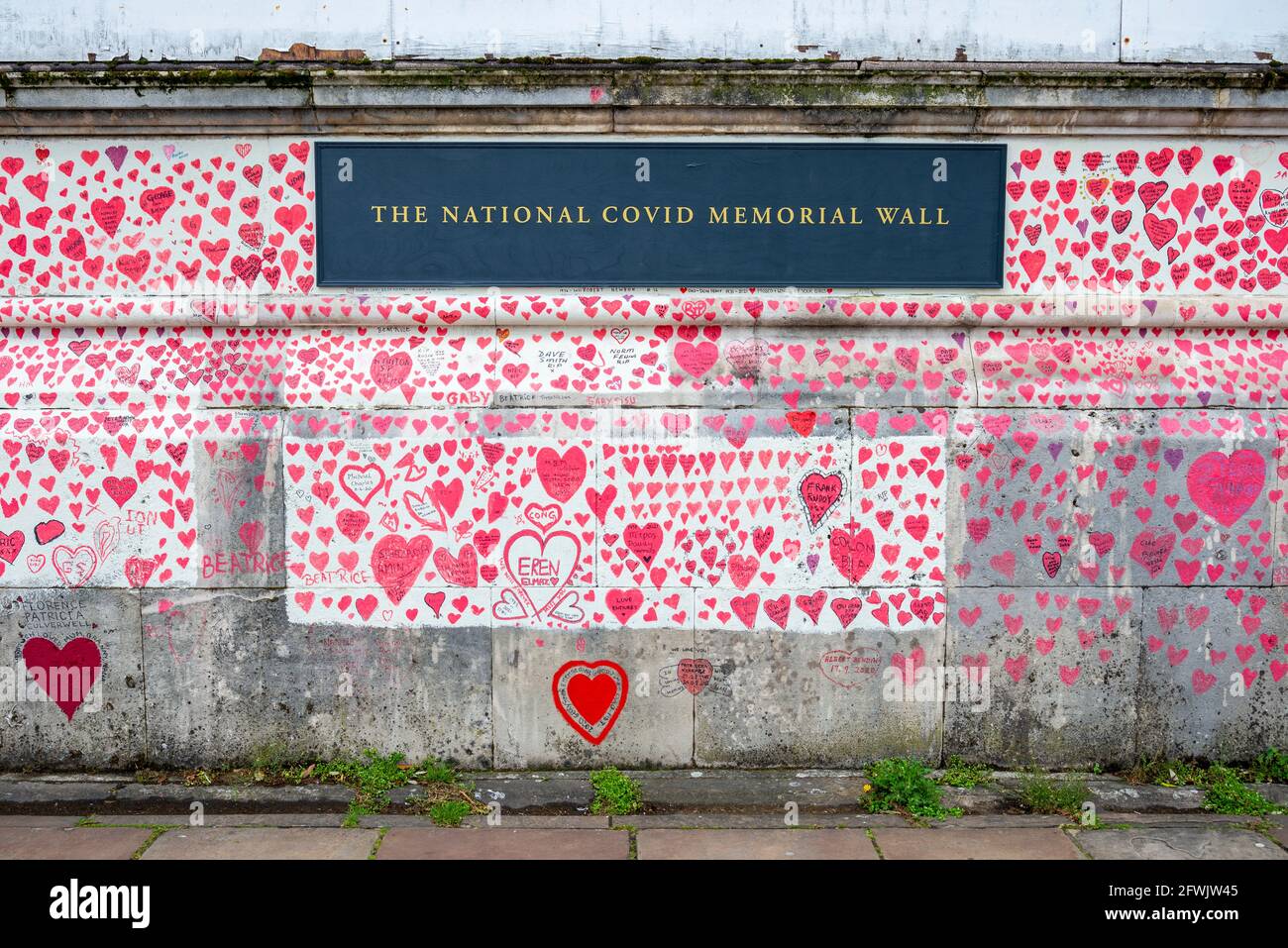 National Covid Memorial Wall in una giornata di lavoro a Lambeth, Londra, Regno Unito. Cuori rossi disegnati su un muro che rappresenta ogni morte di COVID 19. Erbacce Foto Stock