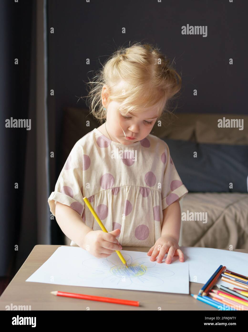 Affascinante bambina prescolare con capelli dorati in lino vestito disegno su pezzo di carta con matite colorate mentre si gioca a casa, tiro verticale. Apprendimento creativo e sviluppo per i bambini Foto Stock