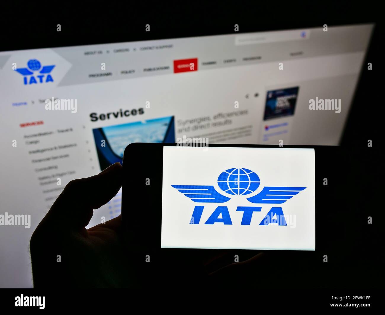 Persona che detiene smartphone con il logo della International Air Transport Association (IATA) sullo schermo di fronte al sito Web. Mettere a fuoco il display del telefono. Foto Stock