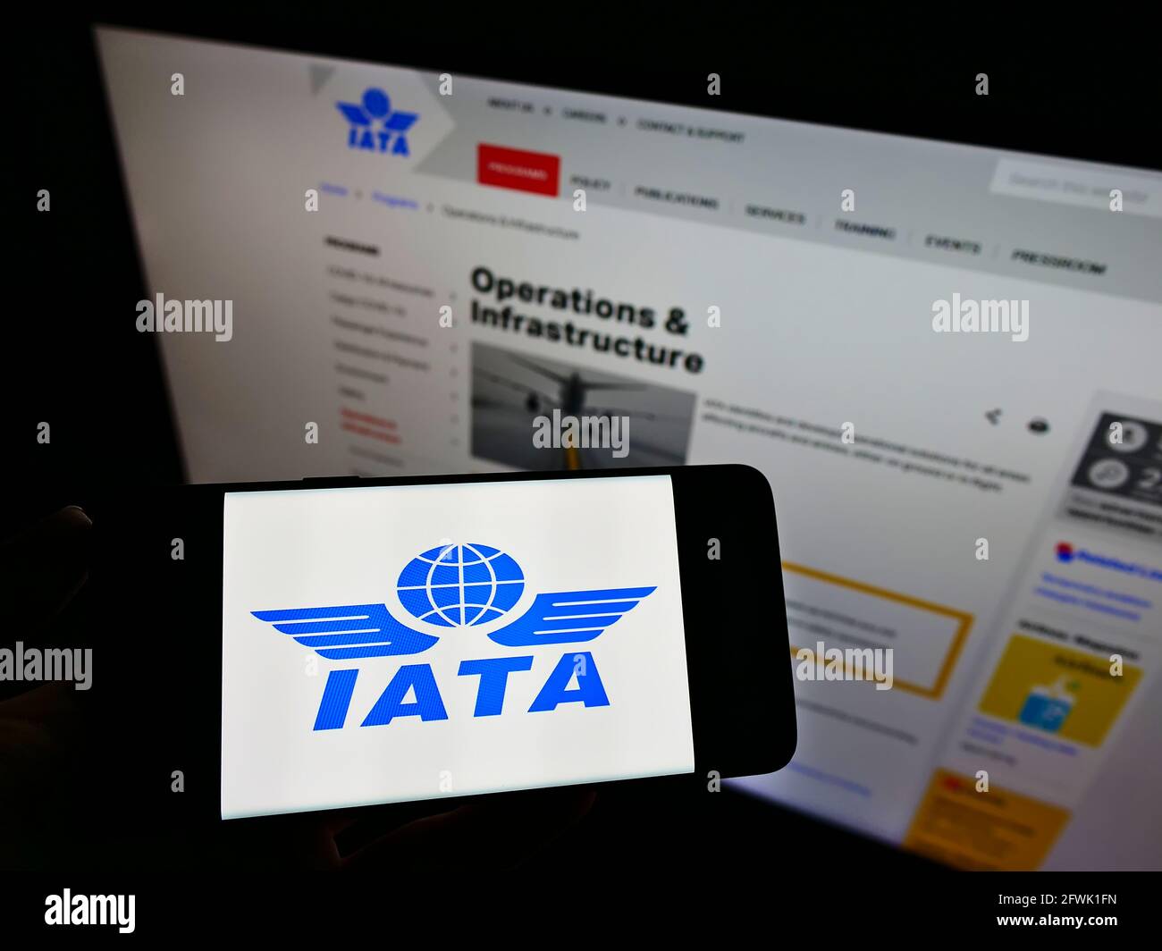 Persona in possesso di smartphone con il logo della International Air Transport Association (IATA) sullo schermo davanti alla pagina Web. Focus sul display del cellulare. Foto Stock