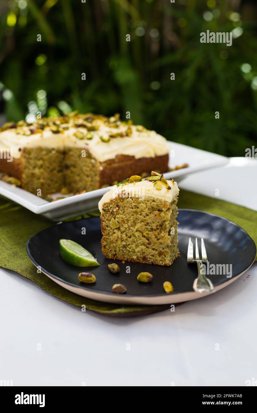 Torta di lime e pistacchio in giardino con una fetta di torta e lime con pistacchi sparsi in primo piano Foto Stock
