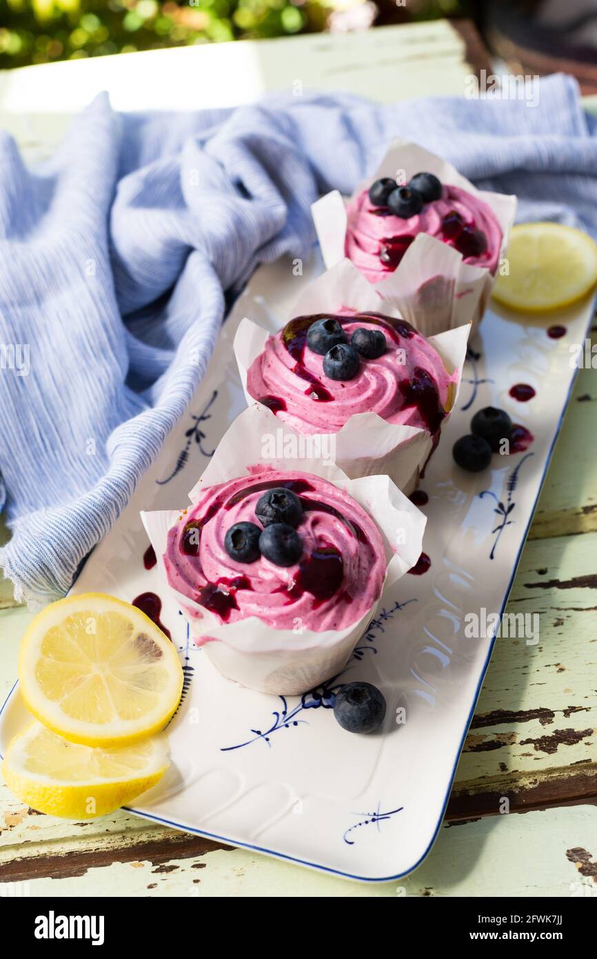 Tre cupcake ghiacciati rosa con mirtilli in giardino Foto Stock