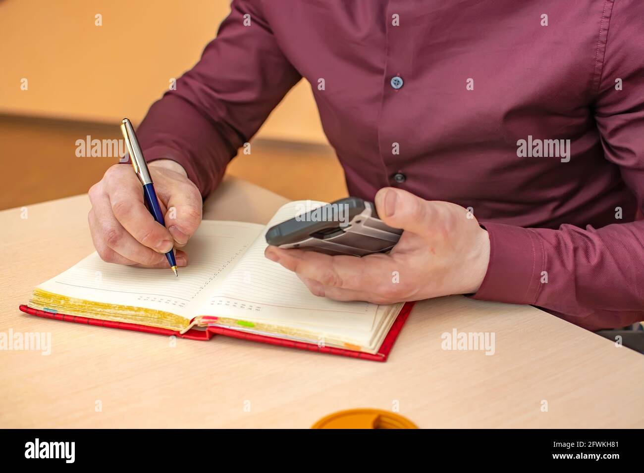 vista della mano di un uomo d'affari con una penna in una stanza d'ufficio, che scrive le note in un notebook Foto Stock