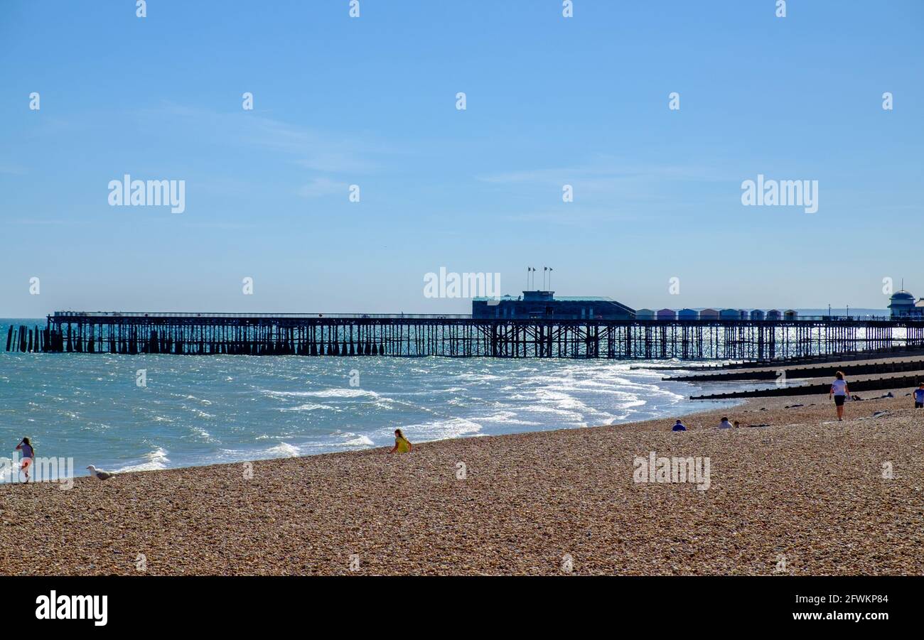 Idea di staycation. Hastings Waterfront con spiaggia di ghiaia, English Channel e Hastings Pier. Persone che si siedono e camminano sulla spiaggia. Sussex orientale, Inghilterra. Foto Stock