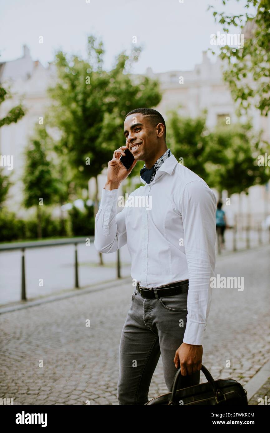 Bel giovane uomo d'affari afro-americano che usa un telefono cellulare mentre attesa di un taxi in attesa di un taxi su una strada Foto Stock