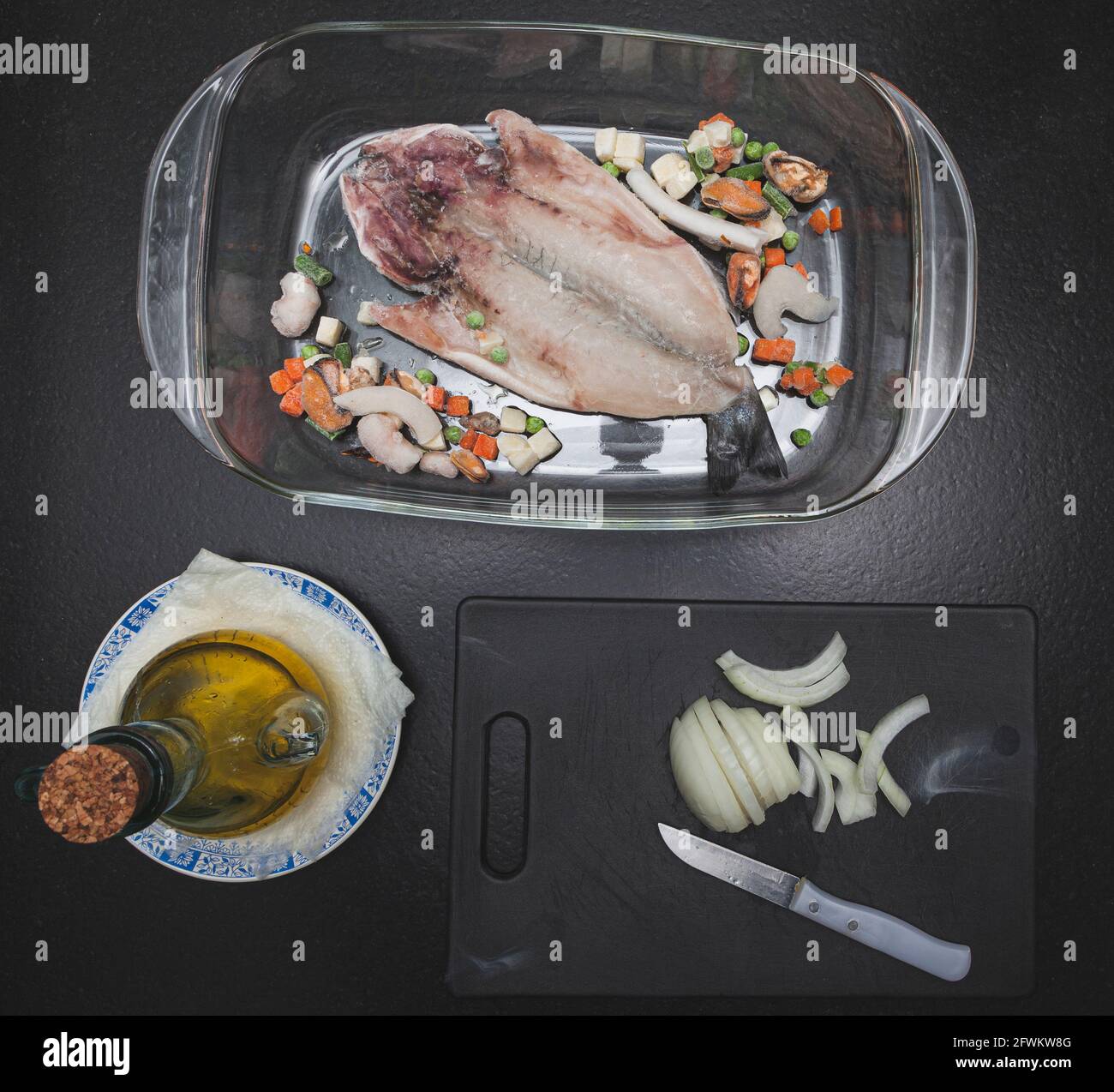 Ricetta per pesce surgelato con verdure e olio, e cipolla tagliata su una  tavola con un coltello preparato per cucinare in forno Foto stock - Alamy