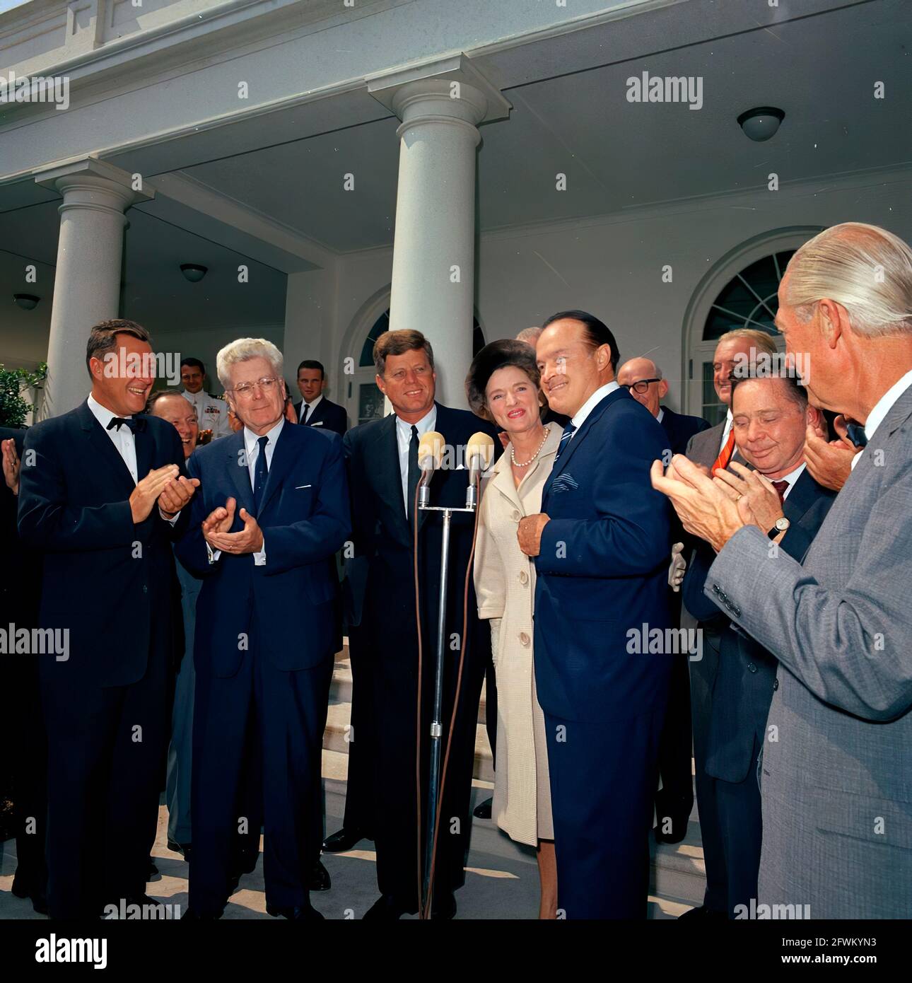 L'attore e comico, Bob Hope, fa commenti dopo aver ricevuto la medaglia d'oro del Congresso, presentata dal presidente John F. Kennedy in riconoscimento dei suoi servizi al paese come intrattenitore durante la seconda guerra mondiale Da sinistra a destra: Non identificato; Rappresentante Michael A. Feighan (Ohio); Presidente Kennedy; moglie di MR. Hope, Dolores Hope; MR. Hope; Unidentified (dietro MR. Hope); Senator Stuart Symington (Missouri); Representative Carl Albert (Oklahoma); Representative Leslie C. Arends (Illinois). Anche nella foto (in piedi a sinistra, sullo sfondo): Aide Navale al presidente, Capitano Shepard. Foto Stock