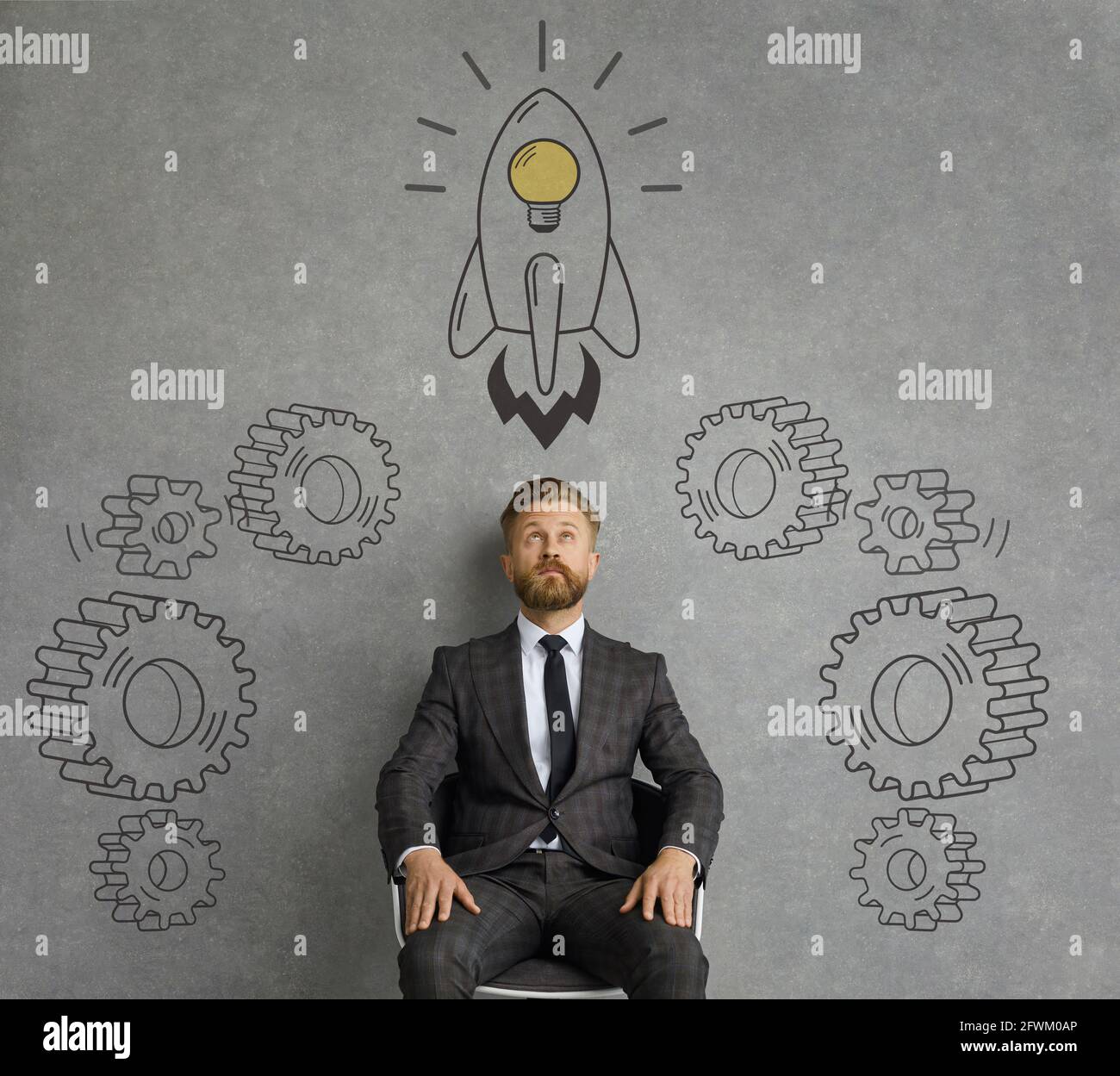 Giovane uomo d'affari che guarda doodles di ingranaggi e razzo volante con lampadina idea Foto Stock