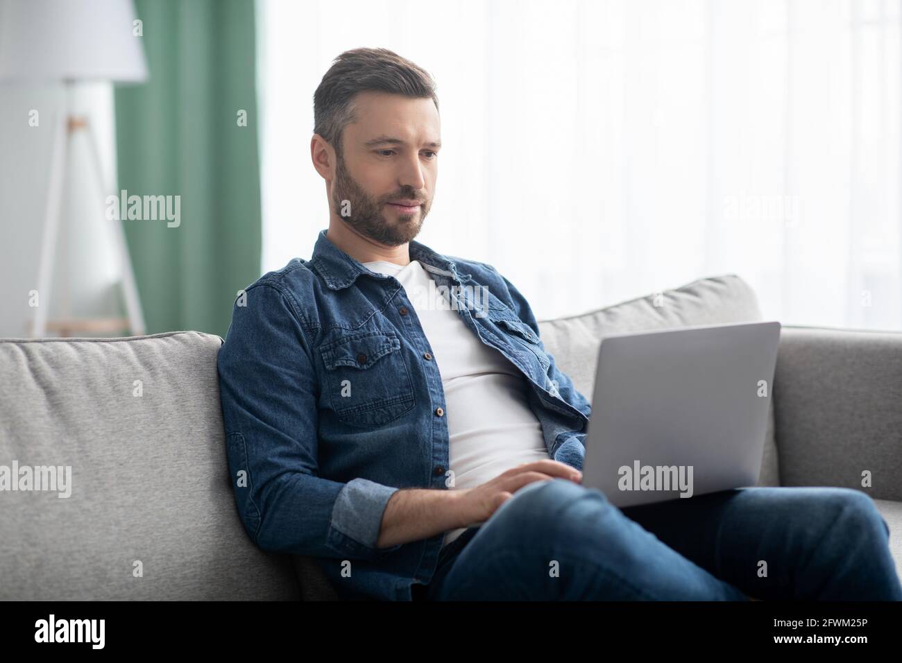 Uomo concentrato che usa il computer, avendo lavoro part-time a casa Foto Stock