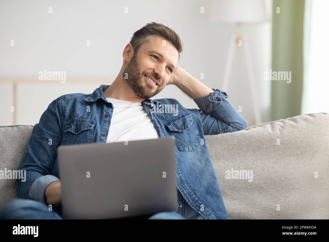 Uomo sognante con il portatore che usa il computer portatile a casa Foto Stock