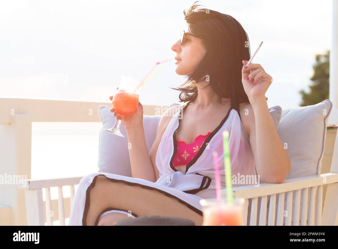 Bella donna di mezza età bere cocktail e fumare su una terrazza vicino al mare Foto Stock