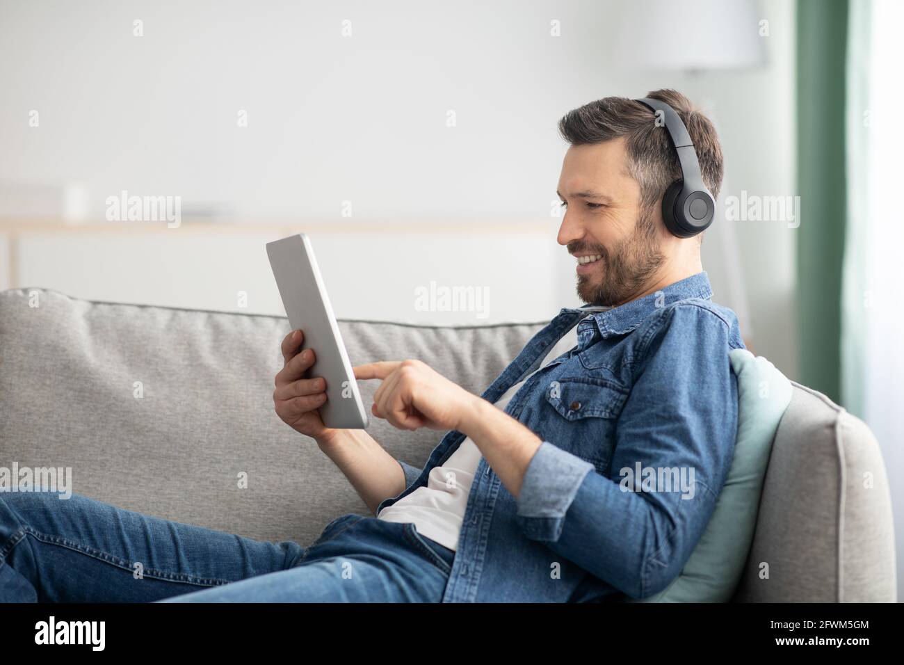 Uomo con la bearded positivo con cuffia e tablet digitale Foto Stock