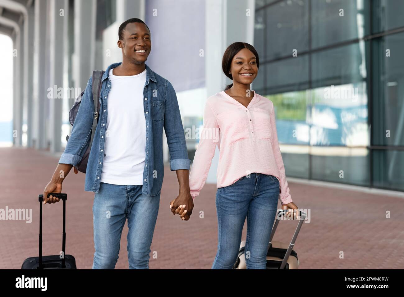 Ritratto di allegra coppia nera tenendo le mani mentre camminando vicino Terminal dell'aeroporto Foto Stock