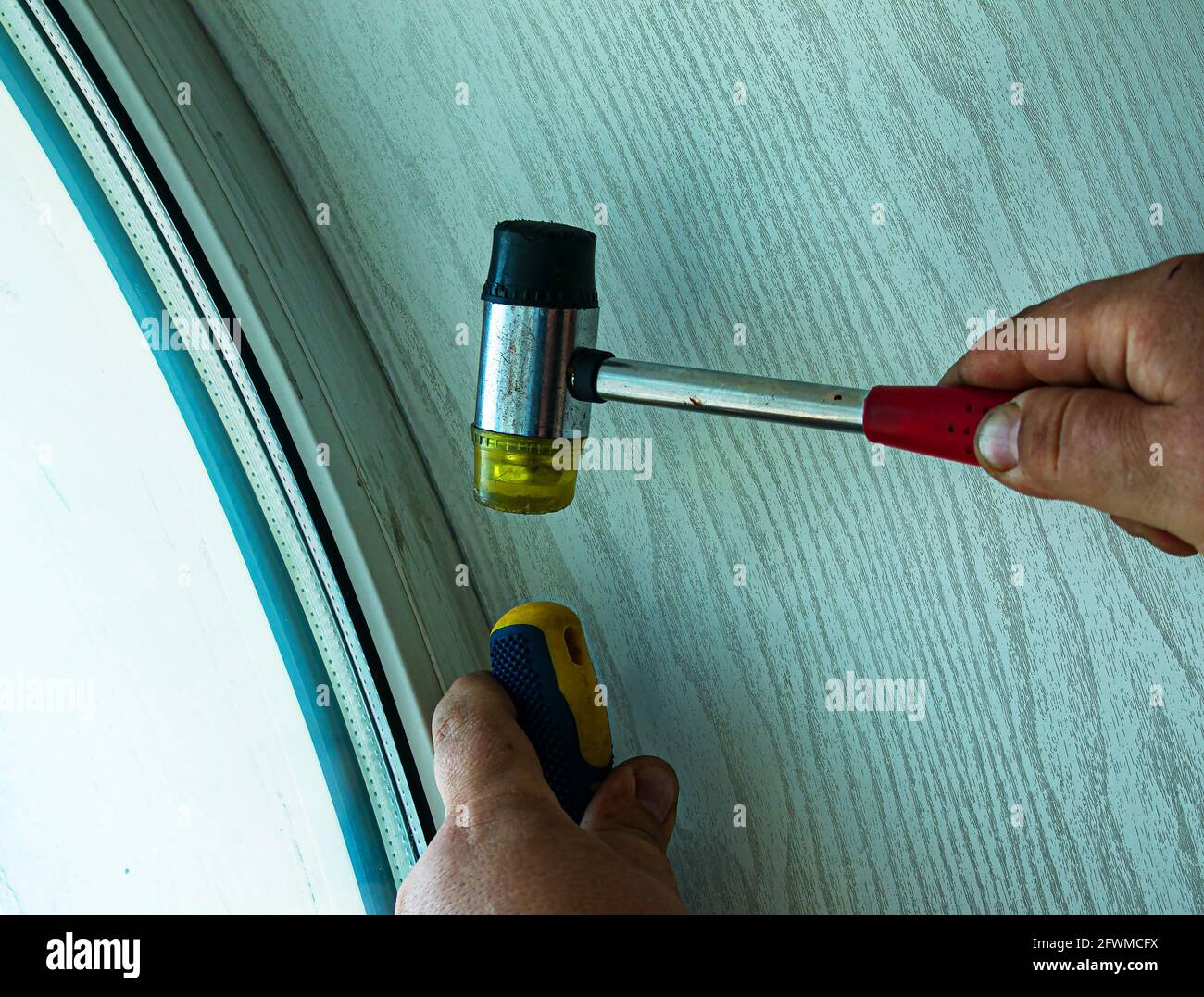 Una persona raddrizza una finestra o una porta in plastica con un cacciavite e un mazzuolo speciale. Le mani maschili si avvicinano. Foto Stock