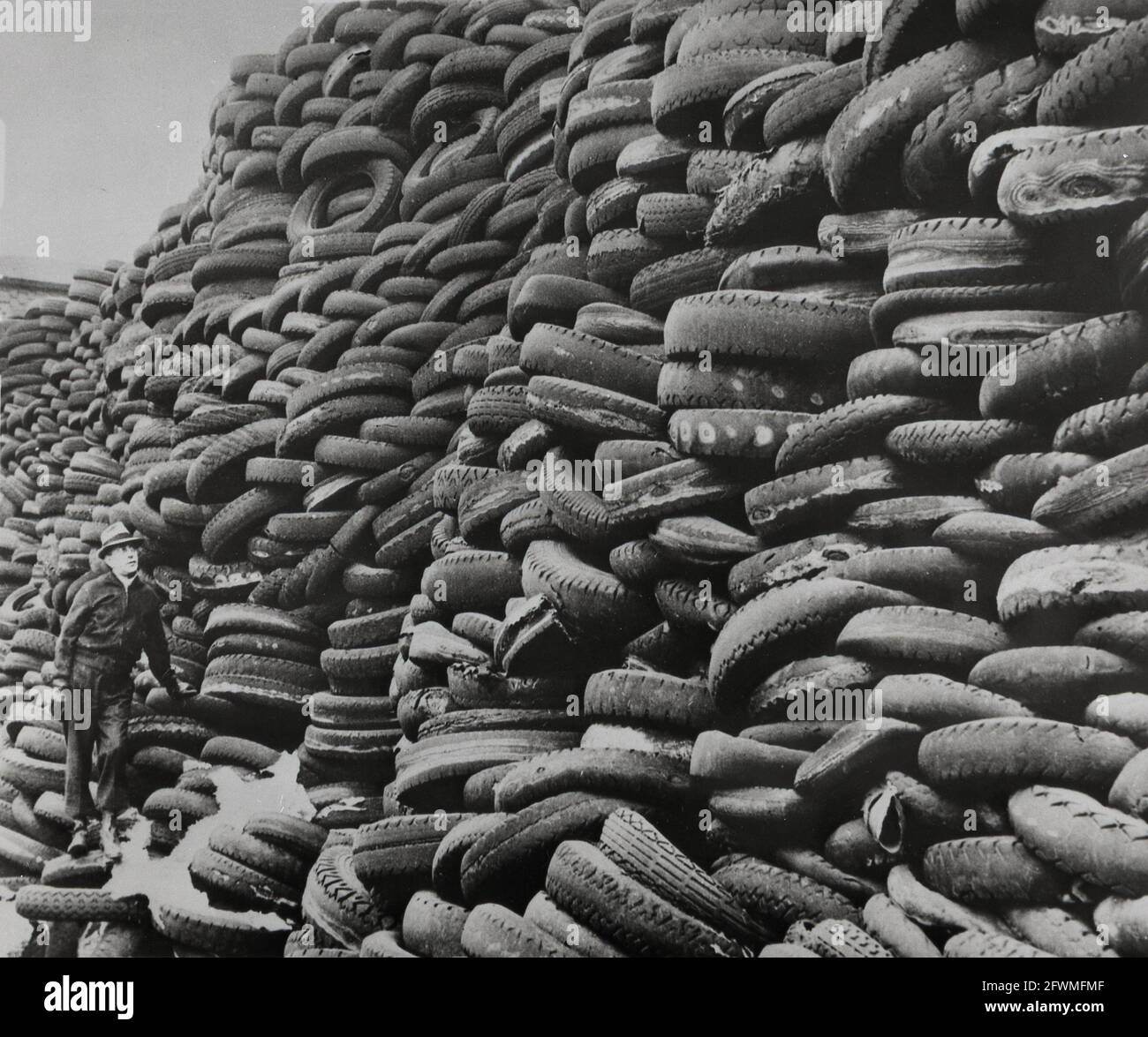 1940 seconda guerra mondiale un uomo non identificato guarda in su mentre si trova ai piedi di un grande mucchio di pneumatici usati dell'automobile, una fonte di gomma rigenerata per uso nello sforzo di guerra Foto Stock