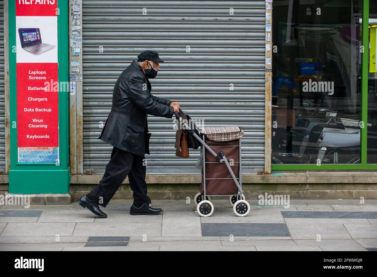 Slough, Berkshire, Regno Unito. 23 maggio 2021. Un anziano spinge il suo trolley lungo Slough High Street oggi. Il tasso di infezione da rotolamento di sette giorni Covid-19 per 100,000 persone in Slough per la settimana che termina il 18 maggio è salito a 25.4, rispetto a 22.7. Dato che il numero di casi positivi di variante indiana di Covid-19 sta iniziando ad aumentare, la possibile eliminazione di tutte le restrizioni di blocco a giugno potrebbe ora essere in pericolo. Credit: Maureen McLean/Alamy Live News Foto Stock