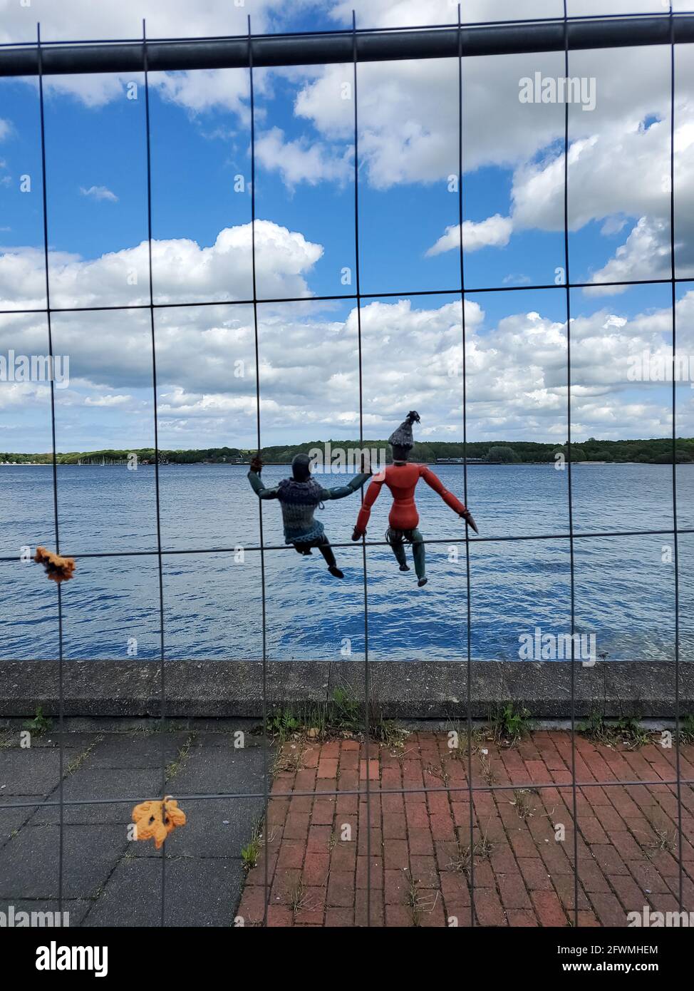 Due piccole figure di legno appese in una recinzione di costruzione dentro Fronte dell'acqua del Mar baltico nel nord della Germania Foto Stock
