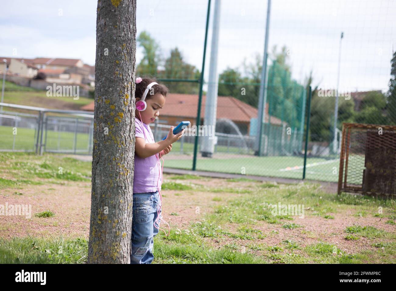 felice latina ragazza utilizzando smartphone e casco sul campo sportivo Foto Stock