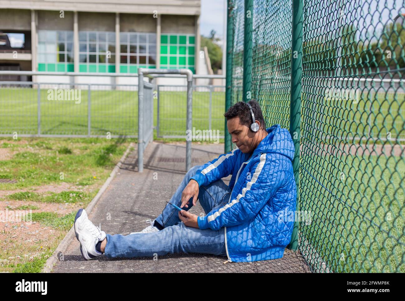giovane latino che ascolta la musica con casco e intelligente telefono in campo sportivo Foto Stock