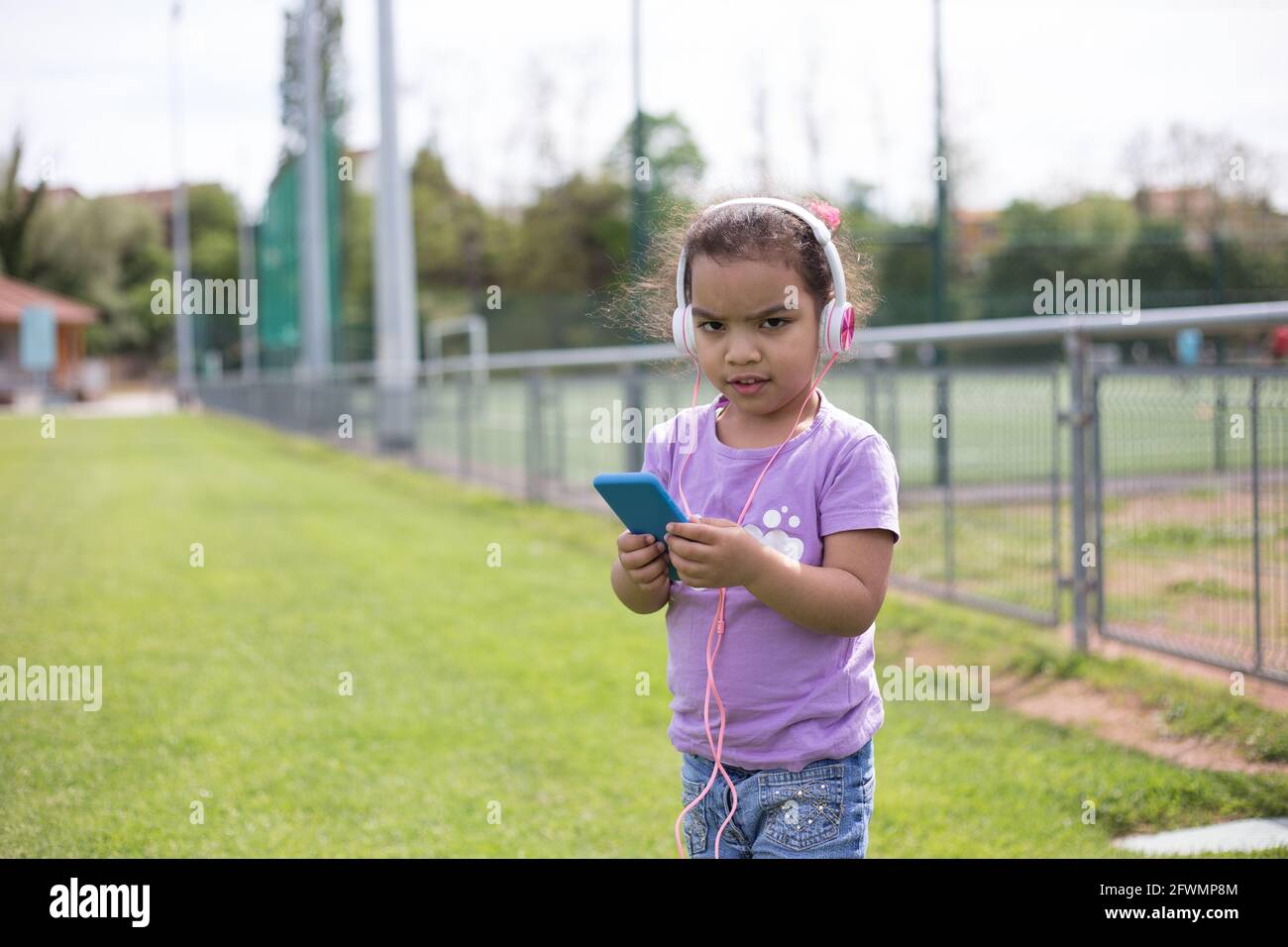 felice latina ragazza utilizzando smartphone e casco sul campo sportivo Foto Stock