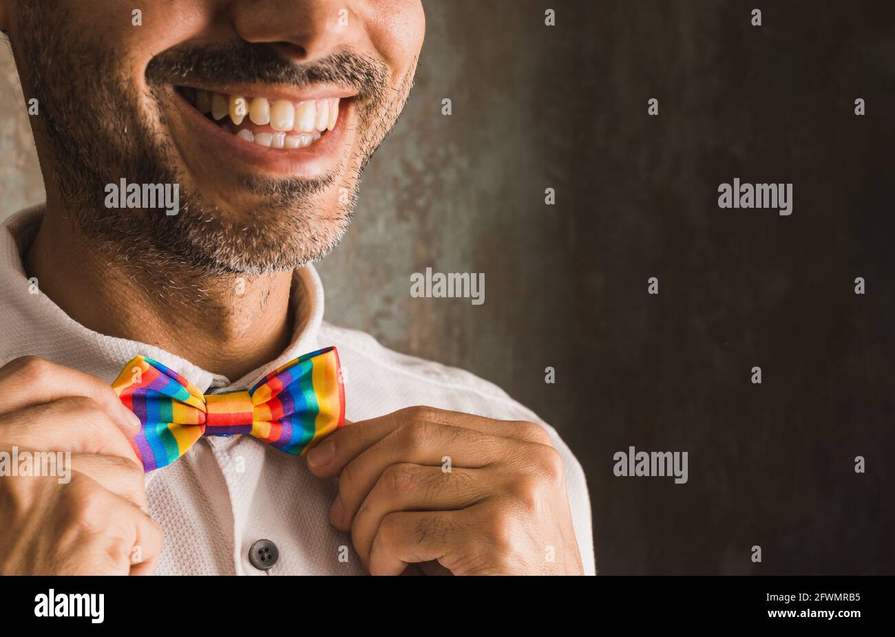 immagine orizzontale di un bruna con barba che sorride in bianco camicia e lgbtqi + cravatta arcobaleno sul lato sinistro di immagine su sfondo usurato illuminato w Foto Stock