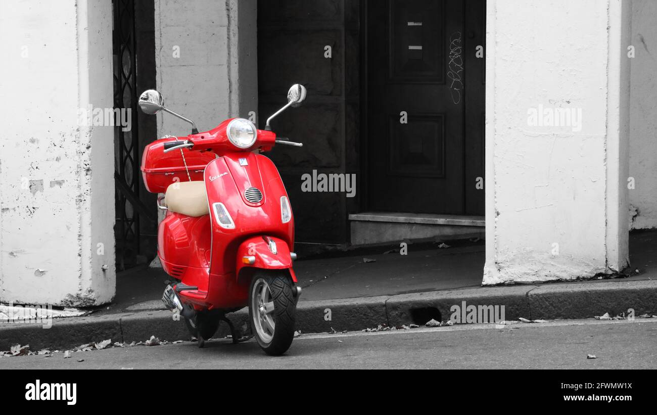 Uno scooter rosso brillante della marca Vespa parcheggiato in una strada cittadina sul lato di una collina. graffiti sullo sfondo. Foto Stock