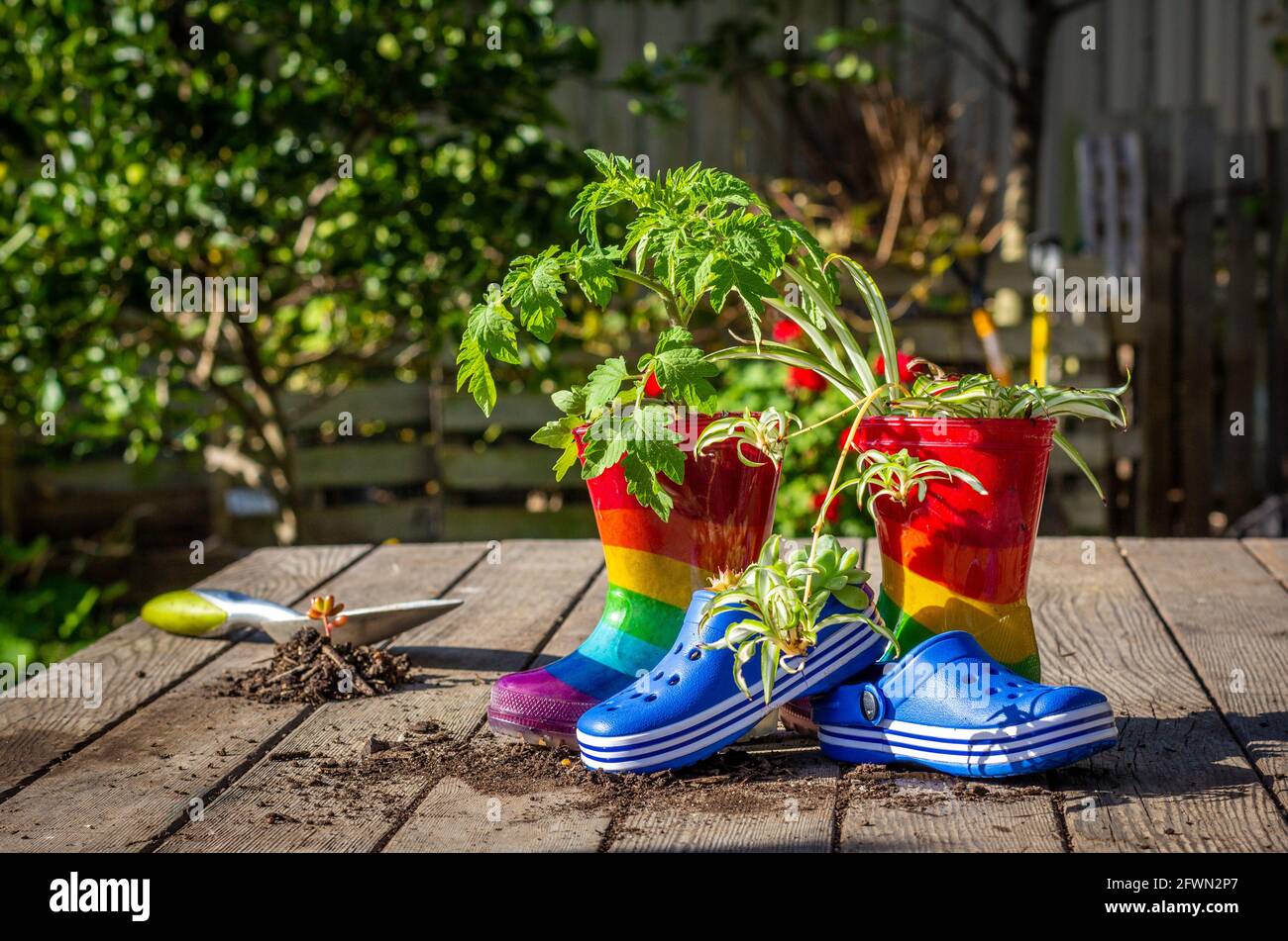 Stivali e scarpe riciclato per bambini sul banco da giardino utilizzato come pentole di piante, un modo divertente per incoraggiare il riutilizzo del riciclo e ridurre gli sprechi. Foto Stock