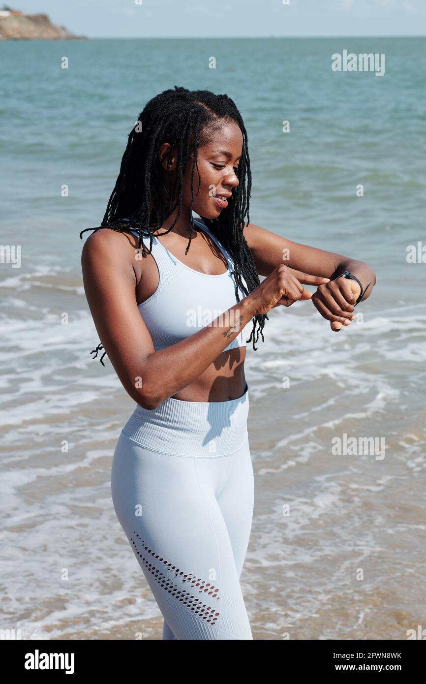 Si adatta giovane donna attraente in piedi sulla spiaggia e controllare smartwatch dopo aver fatto jogging Foto Stock