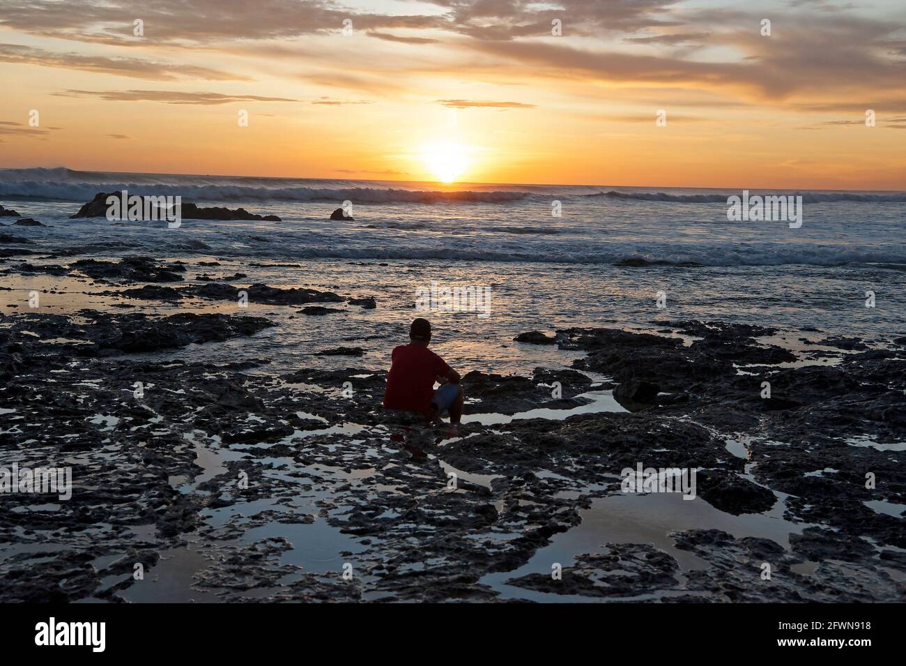 Un uomo che gode di un tramonto colorato da una roccia dentro Piscine in una spiaggia in Costa Rica Foto Stock