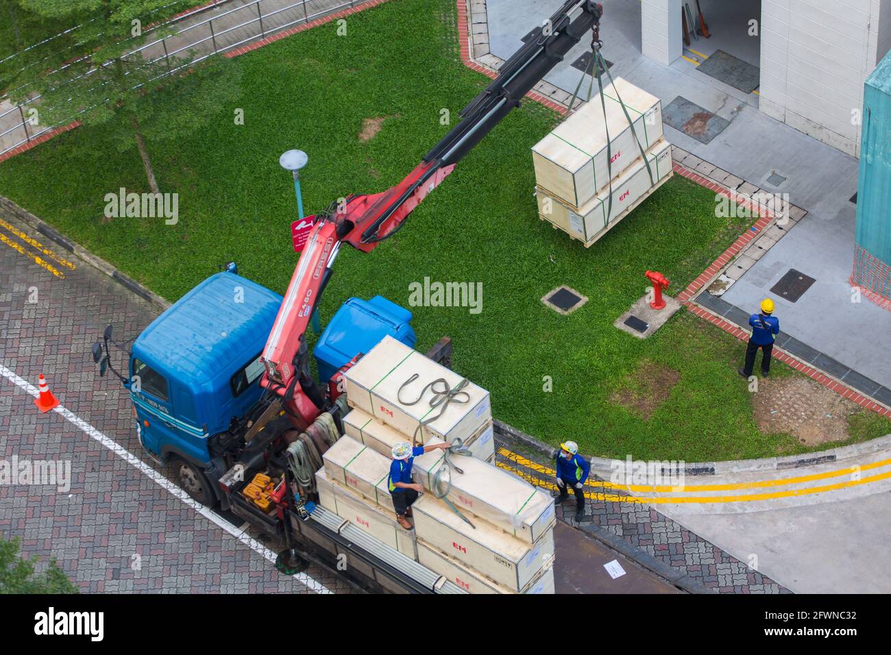 Vista aerea dei lavoratori e dell'operatore sono occupati a scaricare le casse a terra. Singapore. Foto Stock