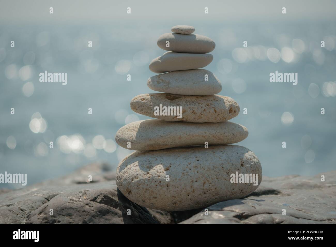Equilibrata piramide di ciottoli sulla spiaggia in una giornata di sole. Abstract Sea bokeh sullo sfondo. Messa a fuoco selettiva. Pietre Zen sulla spiaggia di mare, meditazione Foto Stock