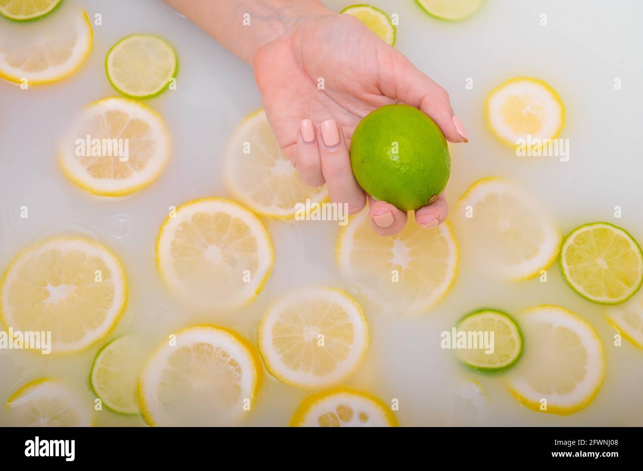 Primo piano di una mano femminile che tiene un calce su bianco acqua con fette di limone Foto Stock