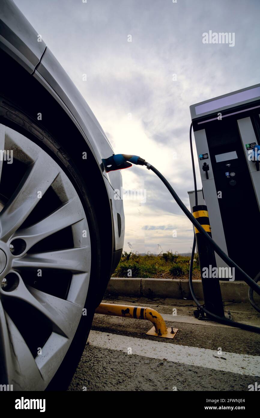 Auto EV collegata al caricabatteria e alla stazione di ricarica EV. Stazione di ricarica per auto elettrica vicino all'autostrada. Auto elettrica. Ricarica dell'auto a emissioni zero. Privo di carbonio Foto Stock