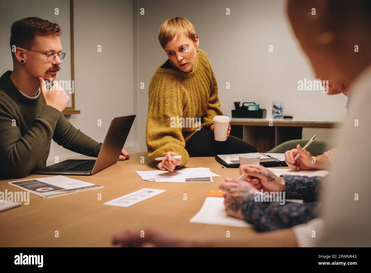 Dirigente femminile che punta alla carta e discute di progetto con il team creativo in riunione. Squadra seduto intorno al tavolo e discutere idee creative in me Foto Stock