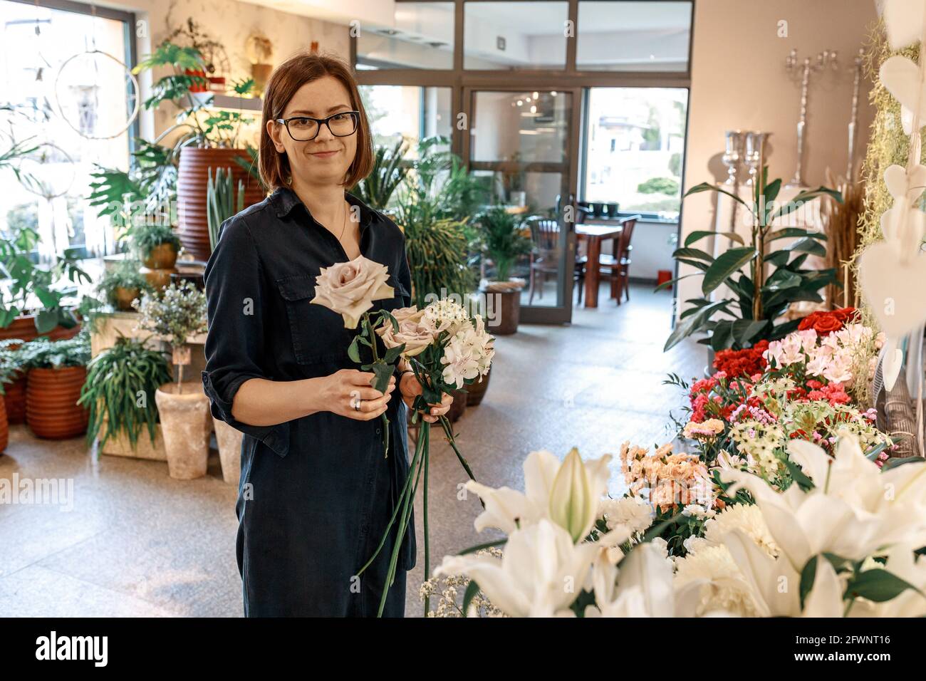 Ritratto di donna bruna con capelli bob e occhiali da indossare nel suo negozio di fiori. Concetto di piccola impresa e hobby Foto Stock